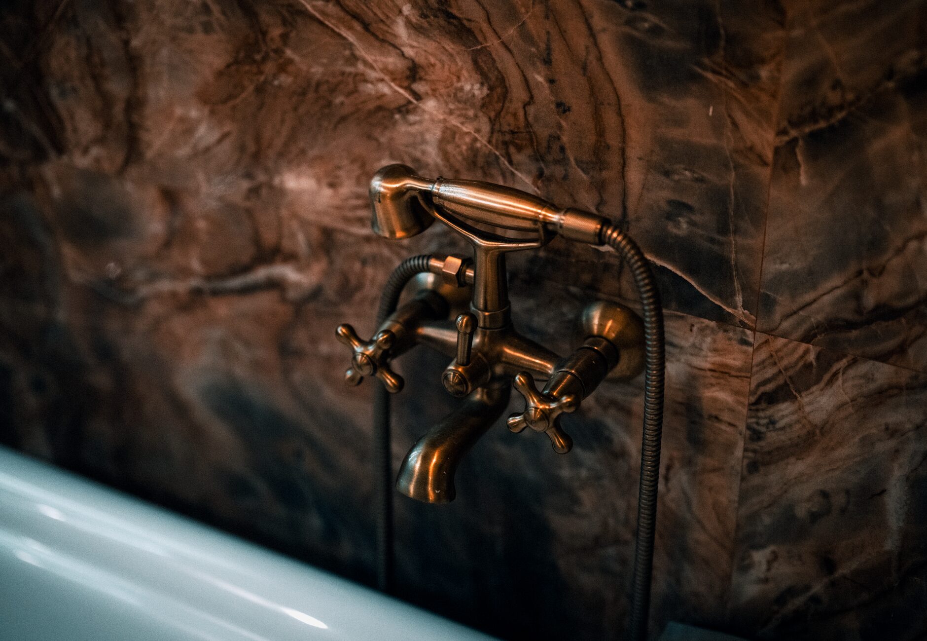Aged warm-brass tub faucet against dramatically veined dark marble