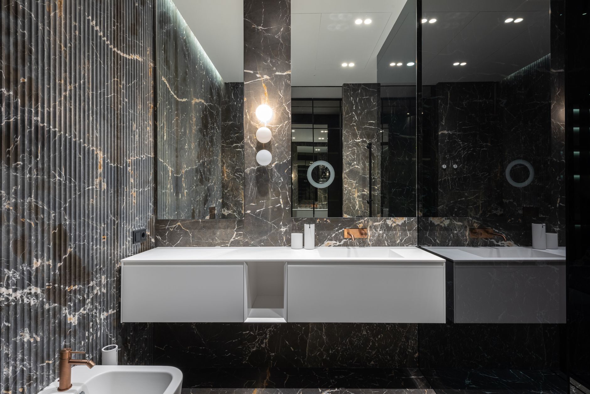 Dark marble and fluted vanity with a warm gold faucet and globe sconce in a luxury restroom