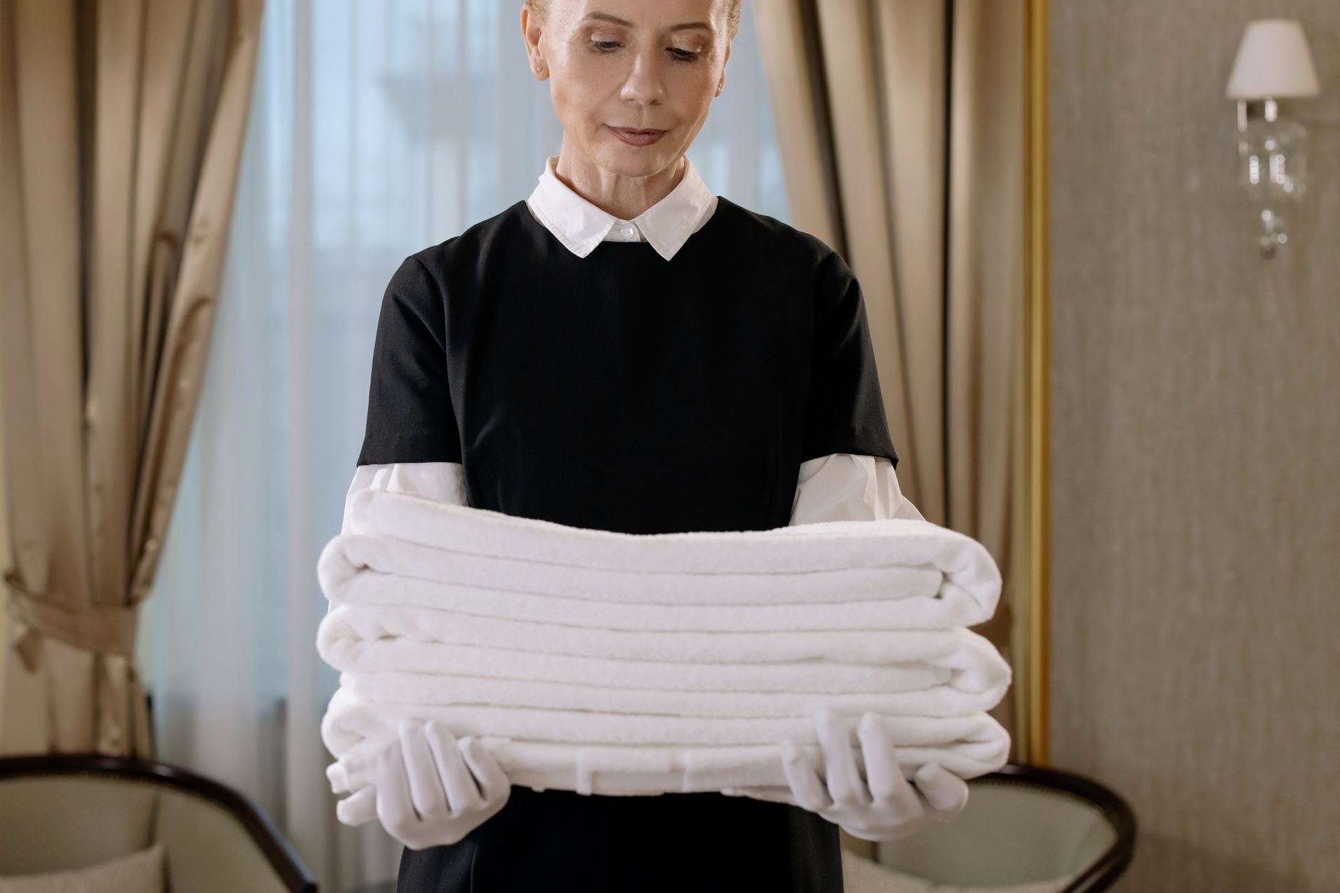 Service professional in a black-and-white uniform holding a perfect stack of folded white towels