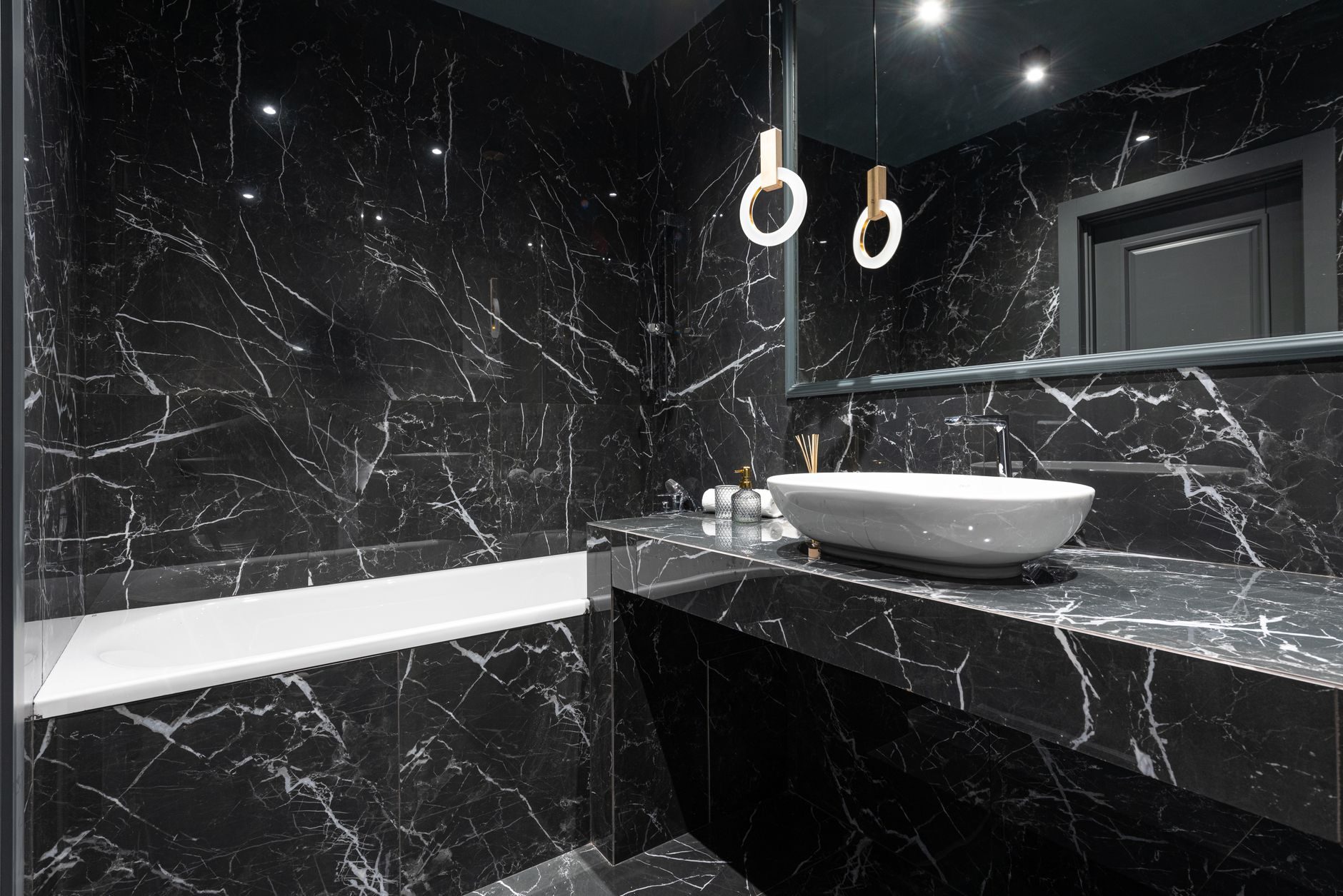 Black Nero Marquina marble bathroom with a white vessel sink and two gold-ringed pendant lights
